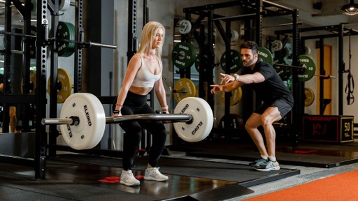 Coach demonstrating correct hip-hinge technique to a client lifting a trap bar during strength training in Dubai