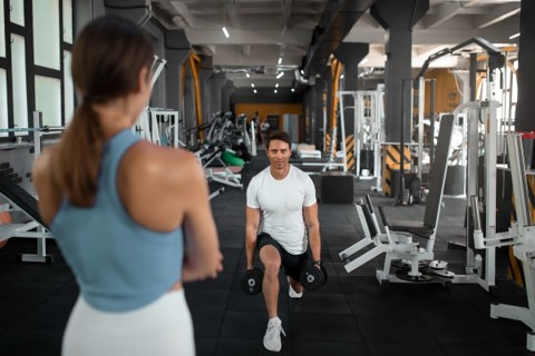 Coach watching a client perform dumbbell lunges, building consistent health habits as part of life coaching in the UAE